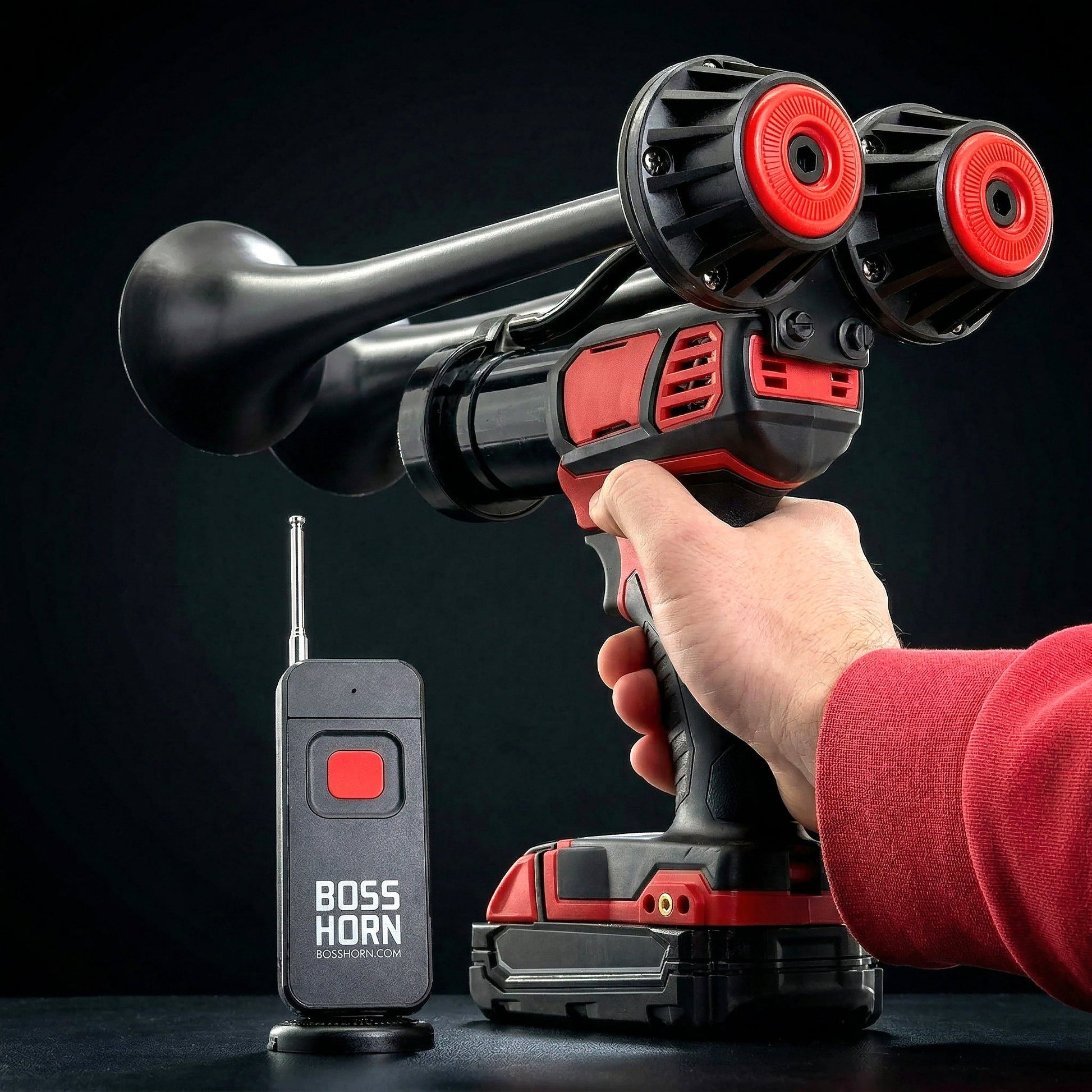 Hand gripping the red cordless power tool firing the black and red dual-trumpet train horn, with wireless remote and Milwaukee® M18 battery