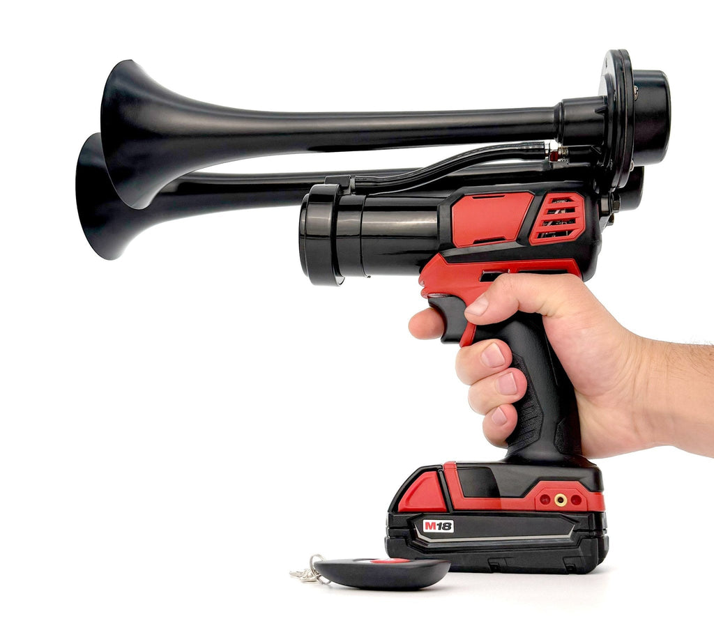 Black dual-trumpet train horn held in hand on a cordless tool with M18 battery, wireless remote in front